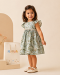 Vestido Helena – Menina em pé com vestido floral azul-sage e cinto de renda
