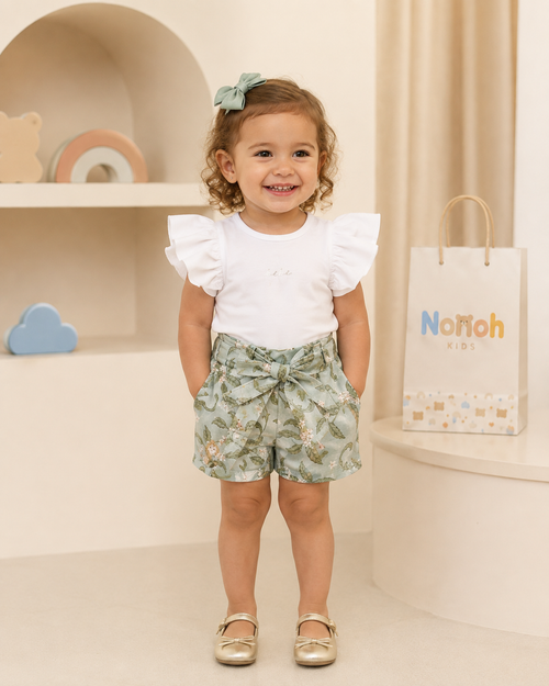 Conjunto Pérolla – Menina em pé com blusa branca babado e shorts floral verde-sage