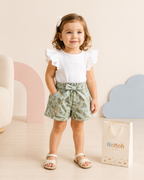 Conjunto Pérolla – Menina sorrindo com mãos nos bolsos do shorts floral